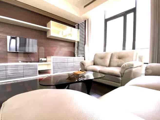 Living area with a modern design, featuring a cream-colored sofa, a glass coffee table, and a wall-mounted TV.