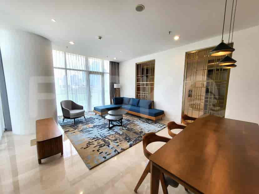 A modern living room featuring a blue L-shaped sofa, patterned rug, and dining area with a wooden table and chairs.