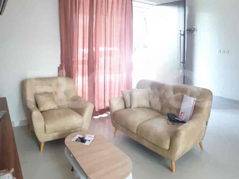 A living room with a tan sofa, an armchair, a coffee table, and a door to the outside.