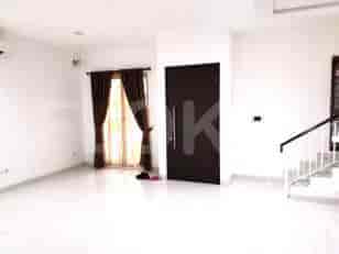 A bright living room with white walls, a dark brown door, and large windows with sheer curtains.