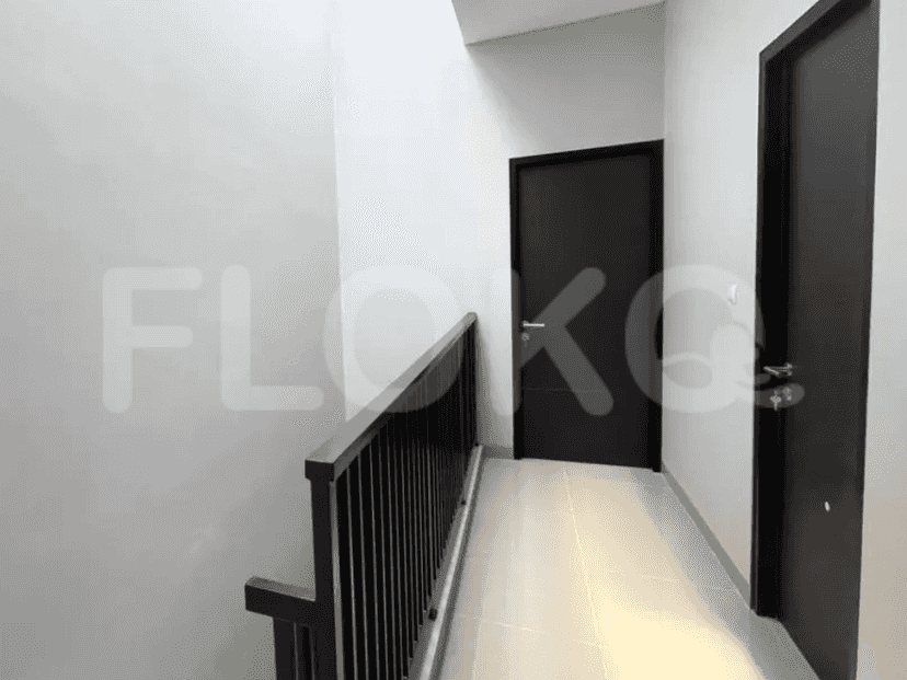 Lorong atas dengan pintu ke kamar, pagar logam hitam, dan dinding berwarna netral.