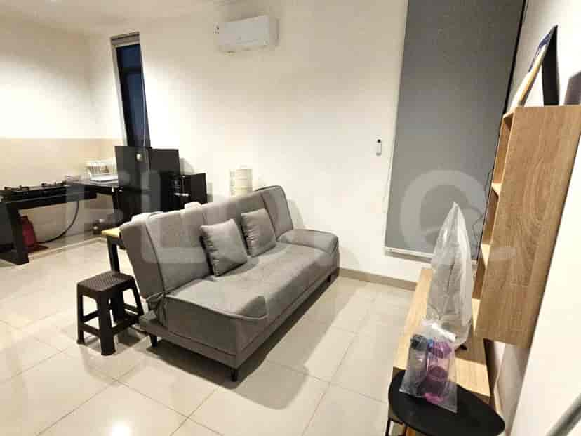Ruang tamu dengan sofa abu-abu, bangku kecil, dan meja.