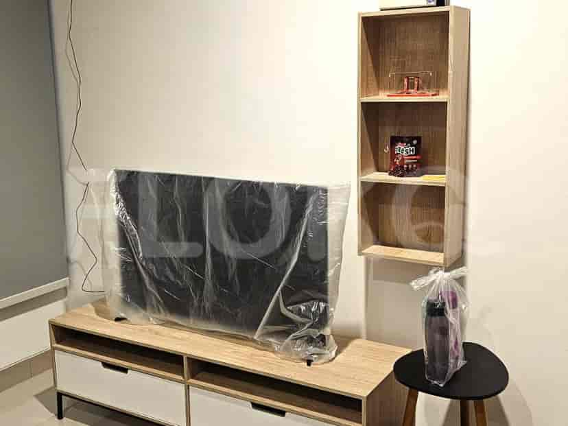 Ruang tamu dengan TV besar, unit penyimpanan kayu, dan bangku hitam kecil.