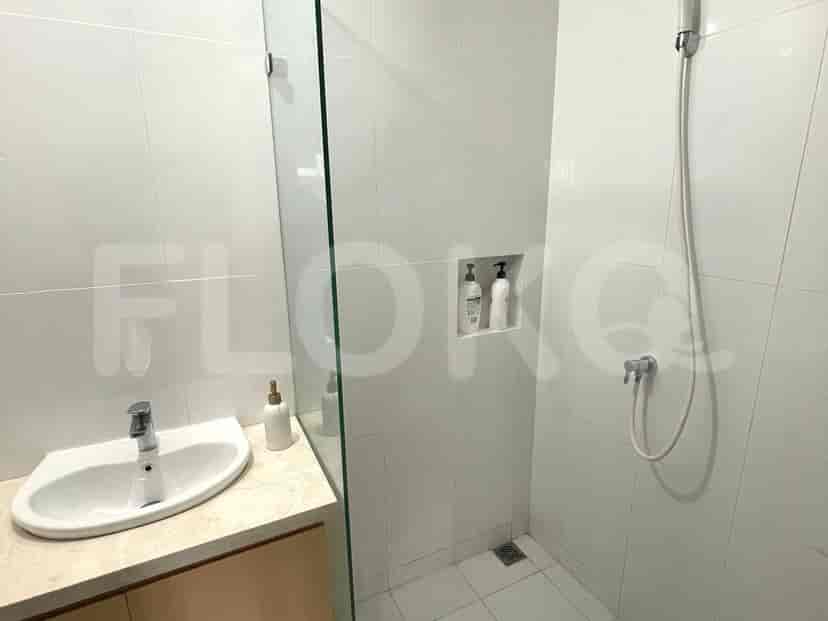 Kamar mandi modern dengan penutup shower kaca, wastafel putih, dan ubin putih.