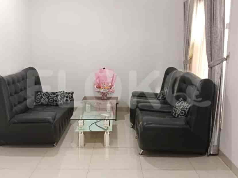 A living room featuring two black leather sofas, a glass coffee table, and a bouquet of flowers.