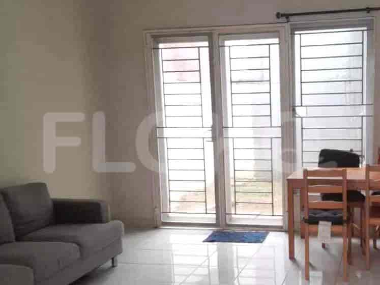 A spacious living room with an L-shaped grey sofa, wall-mounted smart TV, and large window with sheer curtains.