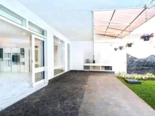 An outdoor patio area with a stone floor, a white wall, and a partially covered ceiling.