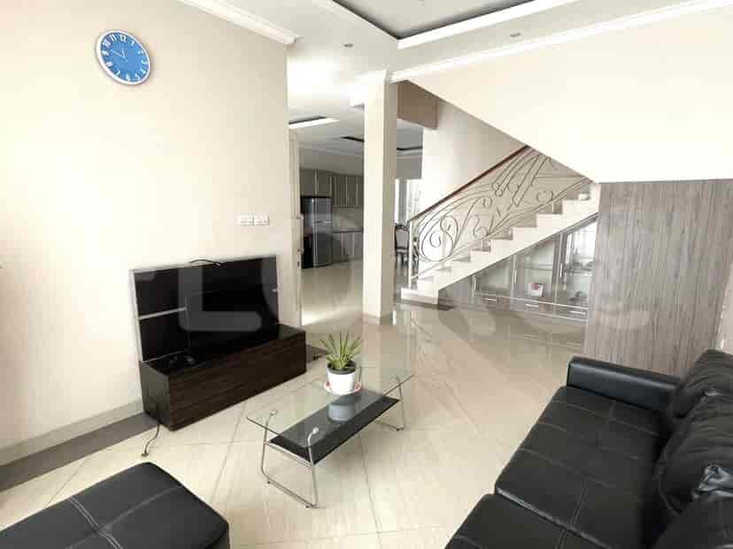 Living room with a black leather sofa, staircase leading upstairs, and a glimpse into the kitchen.