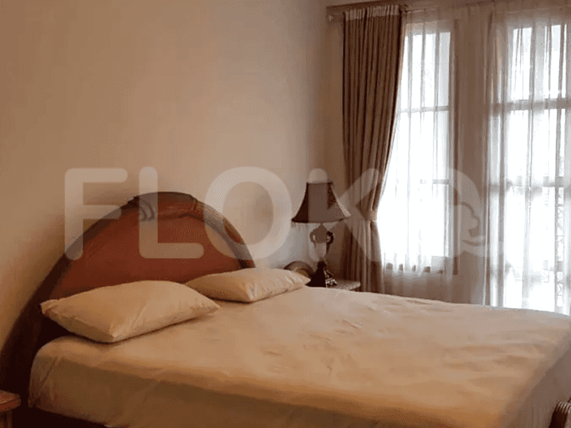 A bedroom with a queen-sized bed, a nightstand with a lamp, and a window with curtains.