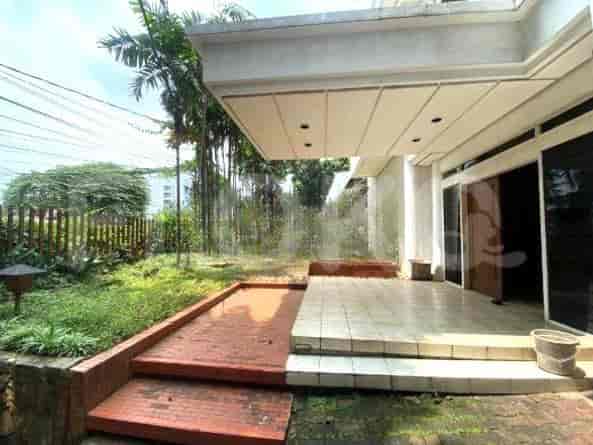 Pemandangan eksterior rumah dengan teras tertutup, jalan setapak bata merah, dan taman dengan pagar.