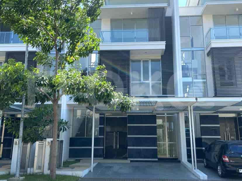 Sebuah rumah tiga lantai modern dengan jendela kaca, balkon, dan sebuah mobil yang diparkir di depannya.