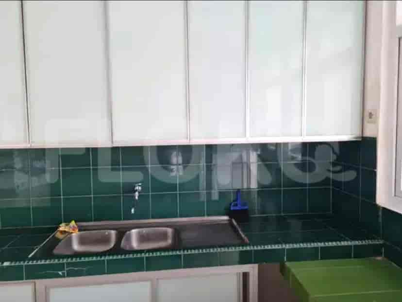 A kitchen with green tiled backsplash, white upper cabinets, and a stainless steel sink.