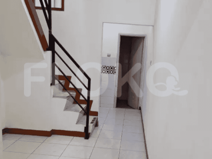 A hallway with white walls, leading towards a door, with a staircase on the side.