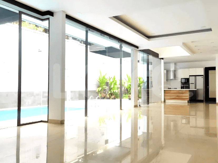 Ruang tamu yang cerah dan terbuka dengan pintu kaca besar yang menghadap ke kolam renang dan tanaman hijau yang rimbun.