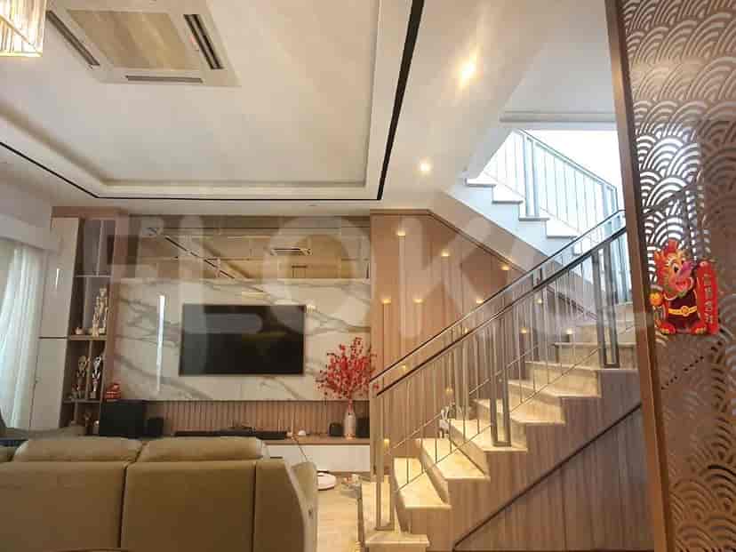 Ruang tamu yang menampilkan TV yang dipasang di atas lemari built-in, tangga, dan dinding dekoratif.