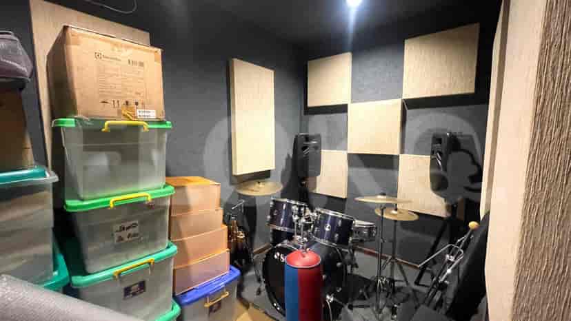 A room setup as a music studio with a drum set, speakers, and soundproofing panels.