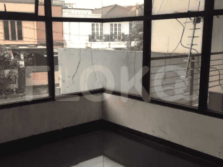 Corner of a room with large windows offering an outdoor view and white walls.