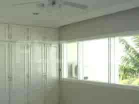 A bedroom with a large built-in wardrobe, a ceiling fan, and a large window with blinds.
