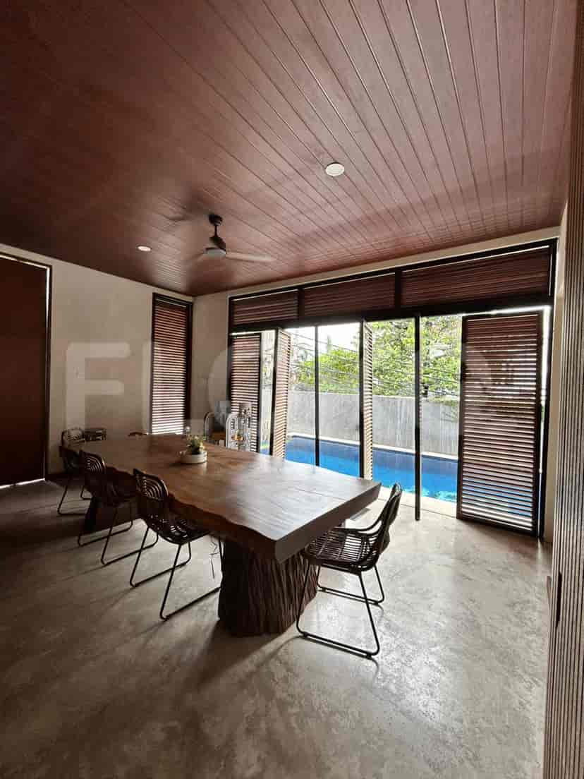 A dining room with a large wooden table, chairs, and a view of the pool.