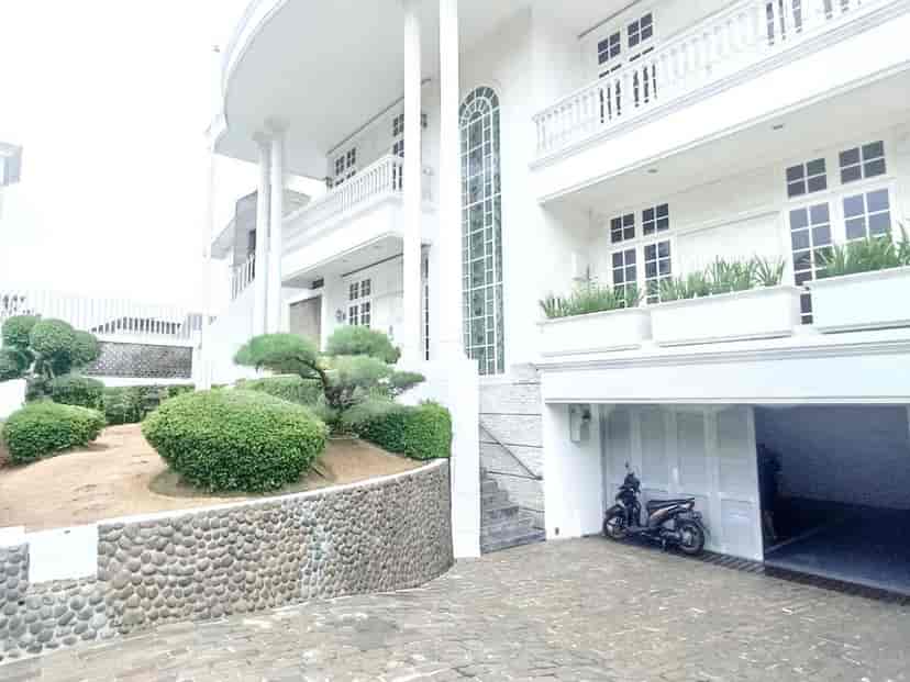 A large, white two-story house with a classic design, featuring a stone-paved driveway, manicured garden, and a scooter parked in the garage.