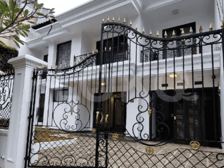 Exterior view of a two-story house with a black wrought iron gate and a paved driveway.