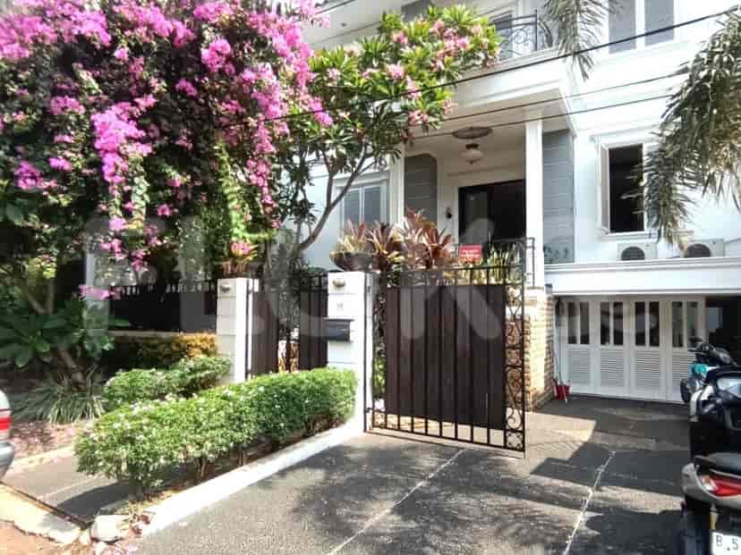 A two-story house with a white facade, a gated entrance, and a lush garden.
