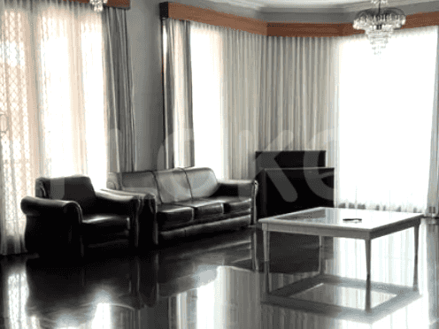 A living room featuring a dark leather sofa and armchair, a glass-topped coffee table, and large windows.