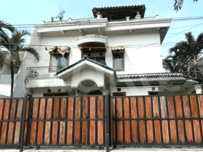 A two-story house with a wooden fence, a large garden, and palm trees.