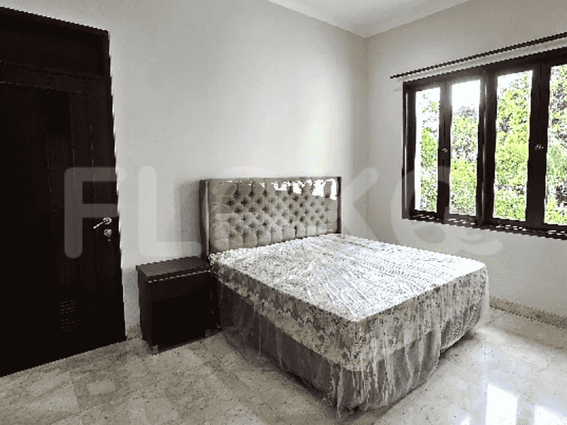 A bedroom with a king-size bed, a nightstand, a large window, and a brown door.