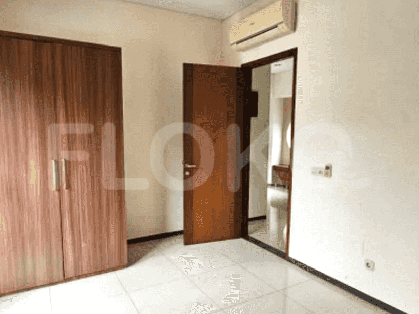 A bedroom with a wooden wardrobe, tiled floors, and a door leading to another room, with a split AC.