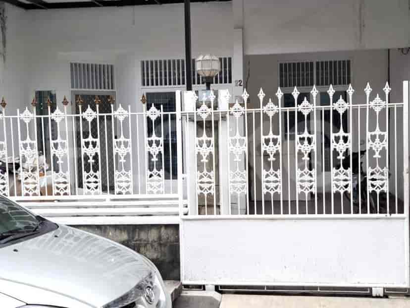 Sebuah rumah putih dengan gerbang logam dekoratif dan mobil yang diparkir di depannya.