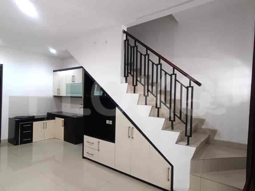 A combined living room and kitchen area with a staircase, white walls, and tiled floors.