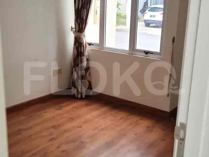 A small, empty bedroom with a window covered by patterned curtains and dark wooden flooring.
