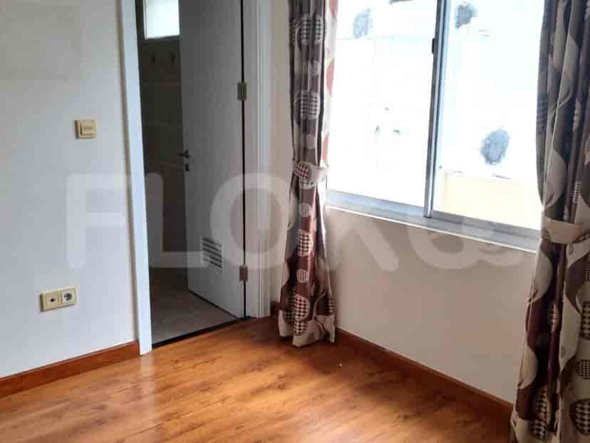 A bedroom with dark wooden flooring, a window with curtains, and an open doorway.