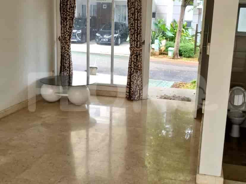 A living room or dining area with light brown flooring, large windows, and a table with a vase.