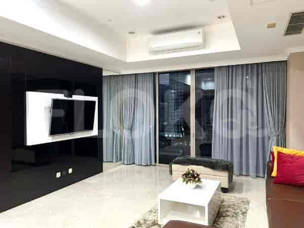 A living room with a wall-mounted TV and large windows with grey curtains.