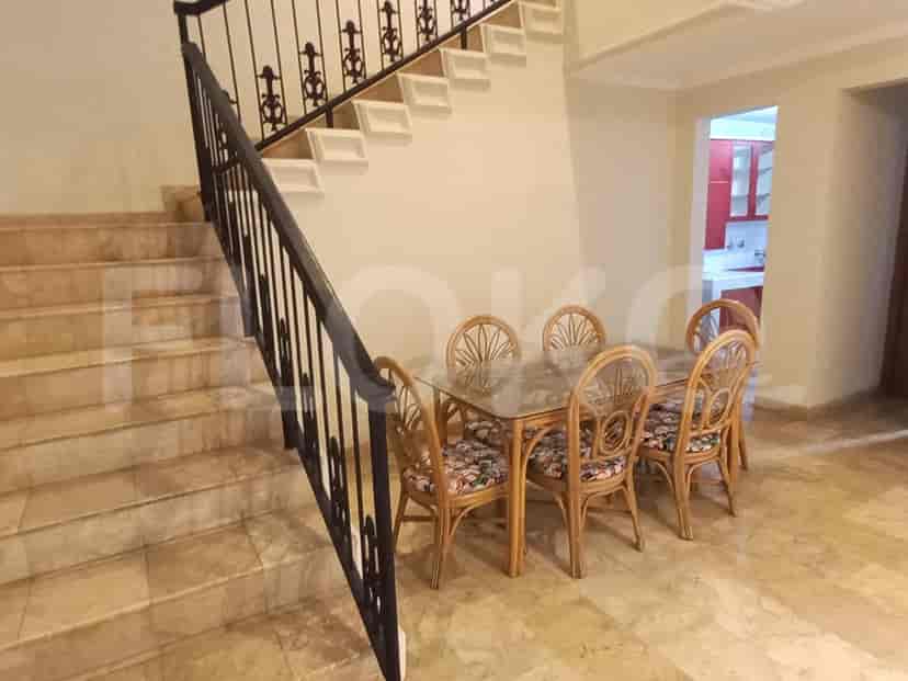 A dining area with a glass-top table and rattan chairs, adjacent to a staircase.