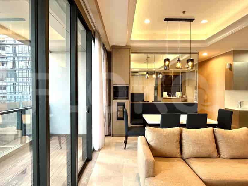 Area tempat tinggal dengan sofa berbentuk L berwarna krem, ruang makan, dan akses balkon.