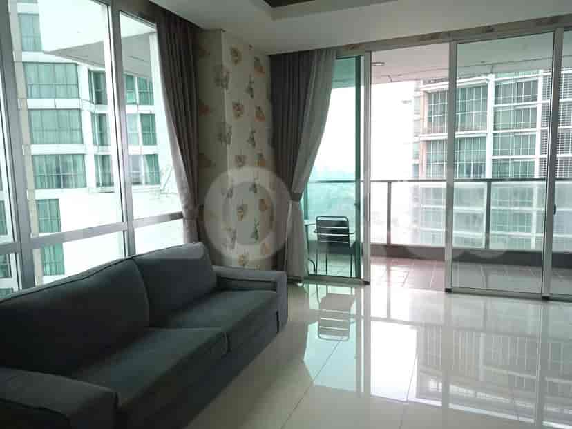 A living room with a grey sofa, a glass door leading to the balcony, and a large window.