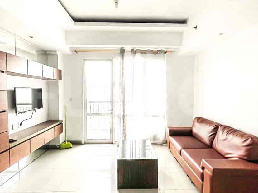 Ruang tamu dengan sofa cokelat, TV, dan meja kopi kaca.