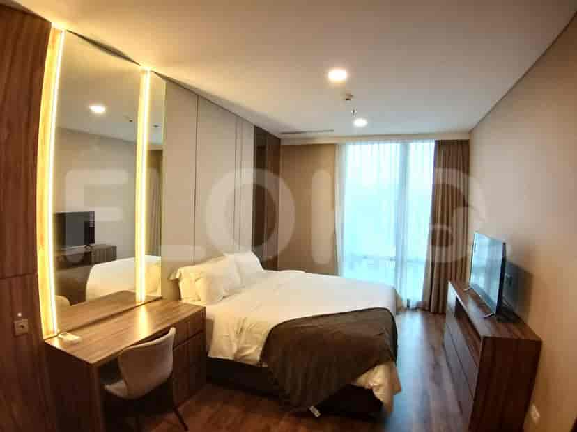 A well-lit bedroom featuring a bed with a brown throw, a dresser with a TV, and a large mirror.