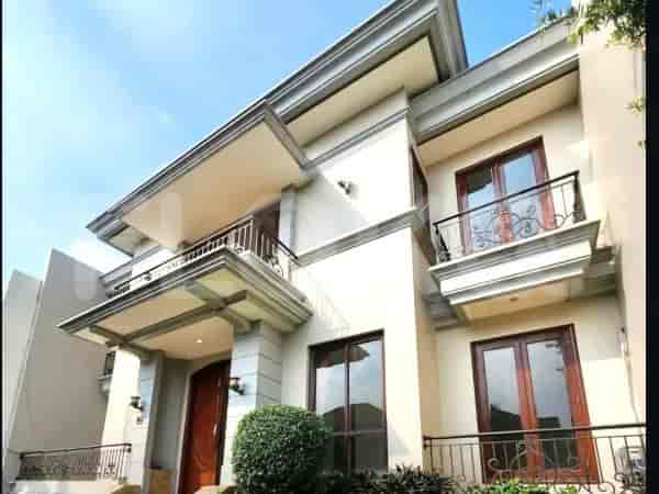 A large, modern house with a light-colored facade, balconies, and a clear blue sky.