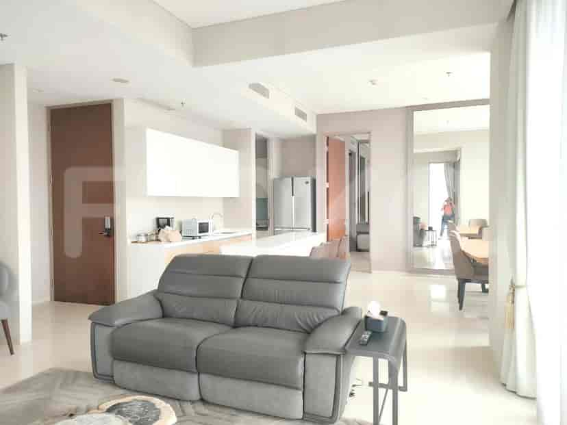 Bright living room with grey leather sofa and open kitchen featuring white cabinetry and stainless steel appliances.