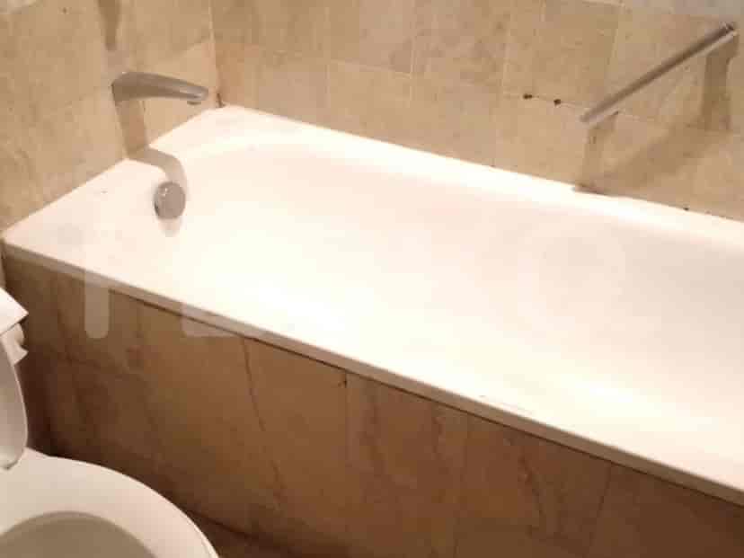 A bathtub with beige tiled walls and a silver faucet.