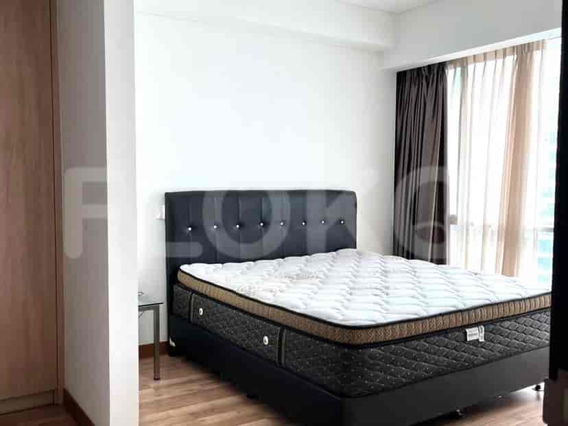Sebuah kamar tidur dengan tempat tidur ukuran king, kepala ranjang berlapis gelap, dan meja samping kaca kecil, di sebelah jendela ber tirai coklat.