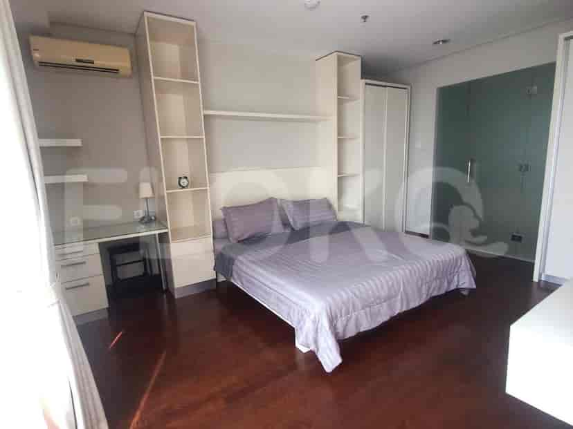 A bedroom with a queen-size bed, built-in shelves, a desk with a chair, and an air conditioning unit.