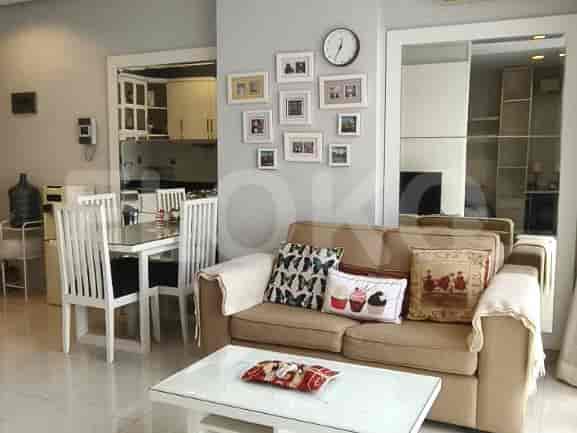A living and dining area with a beige sofa, a glass-top dining table with chairs, and framed pictures on the wall.