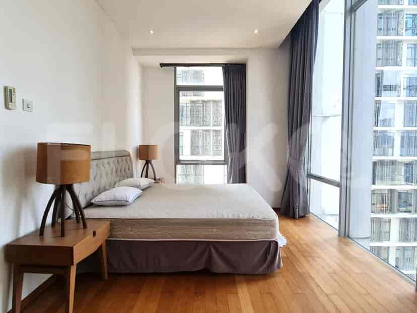 A bedroom with a king-size bed, wooden nightstands, and large windows with curtains.