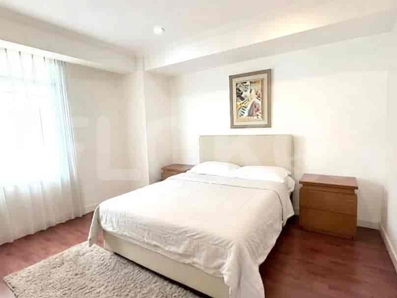 A bedroom with a queen-size bed, two nightstands, and a large window with sheer curtains.