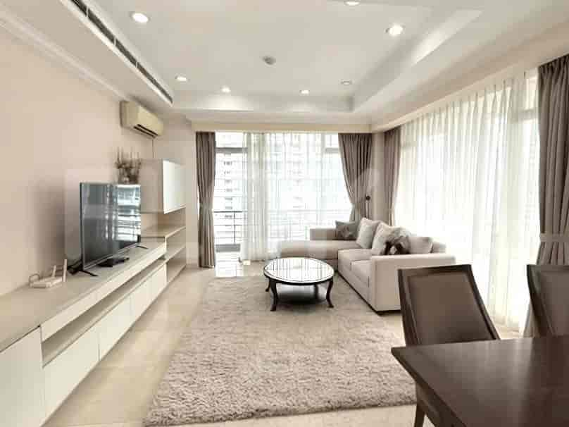 A spacious living room with an L-shaped sofa, a glass coffee table, a long TV console, and large windows with curtains.